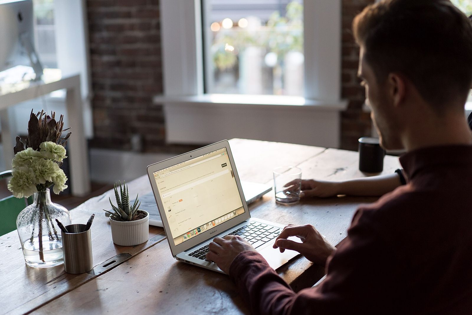 Entwickler arbeitet am Laptop an einem Holztisch am Fenster