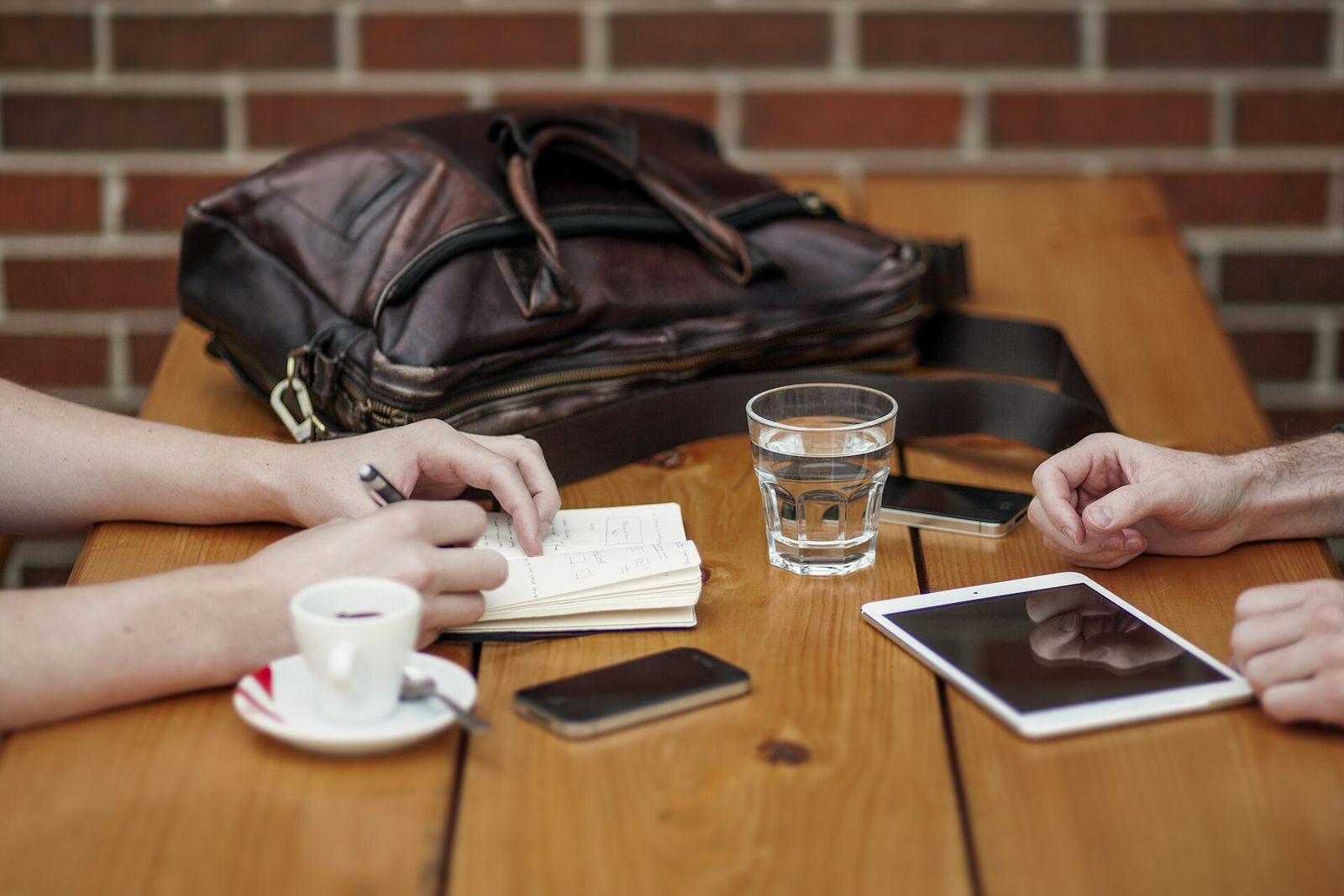 Zwei Personen machen Notizen am Holztisch mit Tablet und Kaffee